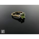 An 18ct peridot and diamond three stone ring, emerald cut claw set peridot flanked by a brilliant