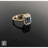 An 18ct hallmarked sapphire and diamond cluster ring, emerald cut sapphire, length 5.8mm, within a