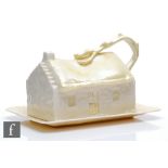 A Belleek butter dish and cover formed as a thatched cottage with a gnarled curling tree forming the