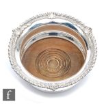 A hallmarked silver bottle coaster of plain form with wooden base and gadroon and leaf border,