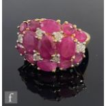A 9ct hallmarked ruby and diamond cluster ring, comprising thirteen oval claw set rubies highlighted
