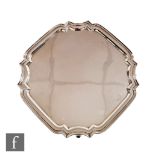 A hallmarked silver canted square salver of plain form with stepped border and raised on four