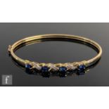 A modern 9ct sapphire and diamond stiff bangle, four oval claw set sapphires spaced by a single