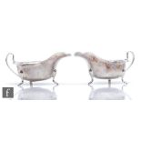 A pair of hallmarked silver sauce boats each raised on three pad feet and terminating in scroll