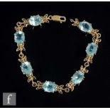 A 9ct hallmarked seven stone blue topaz bracelet, claw set oval stones above leaf design setting