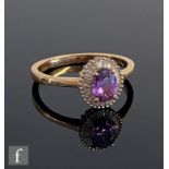 An 18ct purple sapphire and diamond cluster ring, central claw set oval sapphire within a border