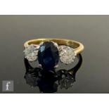 An 18ct sapphire and diamond three stone ring, central claw sapphire, length 9mm, flanked by a