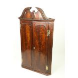 A George III period mahogany Hanging Corner Cupboard, with moulded swan neck pediment above two