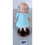 German doll on stand, painted hair with blue bows, painted socks & shoes. Blue dress. 6” high