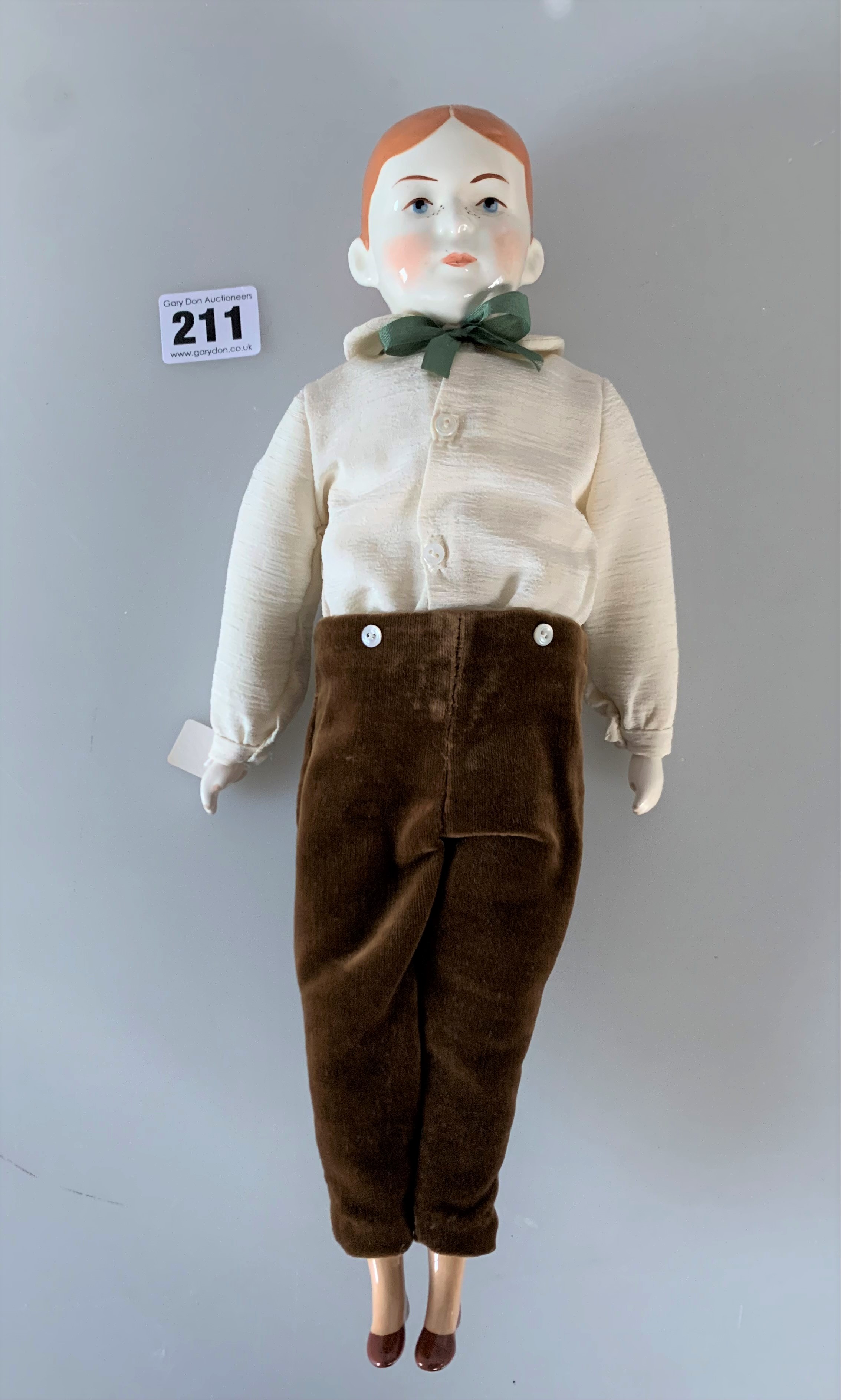 China boy doll dressed in brown velvet trousers, cream shirt, green tie. 13” high