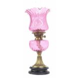 Victorian brass and cranberry glass font oil lamp with fluted flared shade, raised on pottery