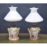 Similar pair of Sitzendorf figural porcelain oil table lamps, modelled with cherubs supporting the