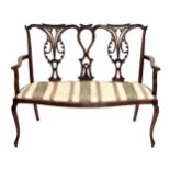 Mahogany double chair back settee, with carved stylised open splats, over a stuff over bench seat on