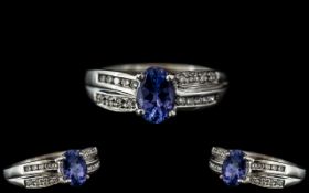 A Platinum Diamond Ring set with an oval blue faceted stone between channel set round brilliant cut