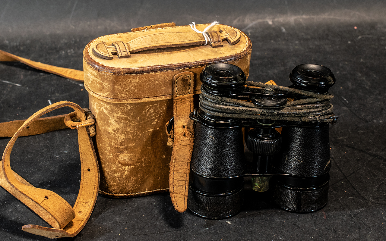 Pair of Binoculars housed in a tan leather case with carrying strap.