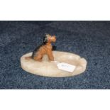 A marble or onyx ashtray mounted with a painted model of a seated Airedale Terrier.