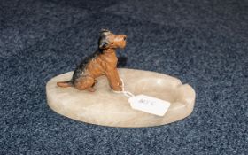 A marble or onyx ashtray mounted with a painted model of a seated Airedale Terrier.