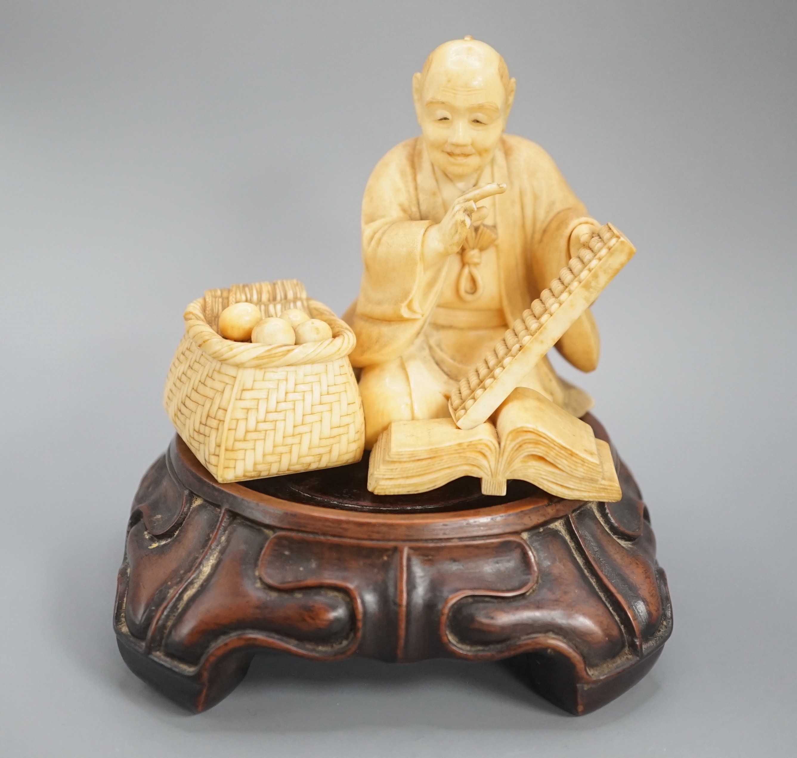 A Japanese ivory okimono of a street vendor kneeling and holding an abacus, Meiji period, 8cm,
