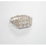 A white metal and nine stone diamond set tablet ring, with diamond set stepped shoulders, size K,