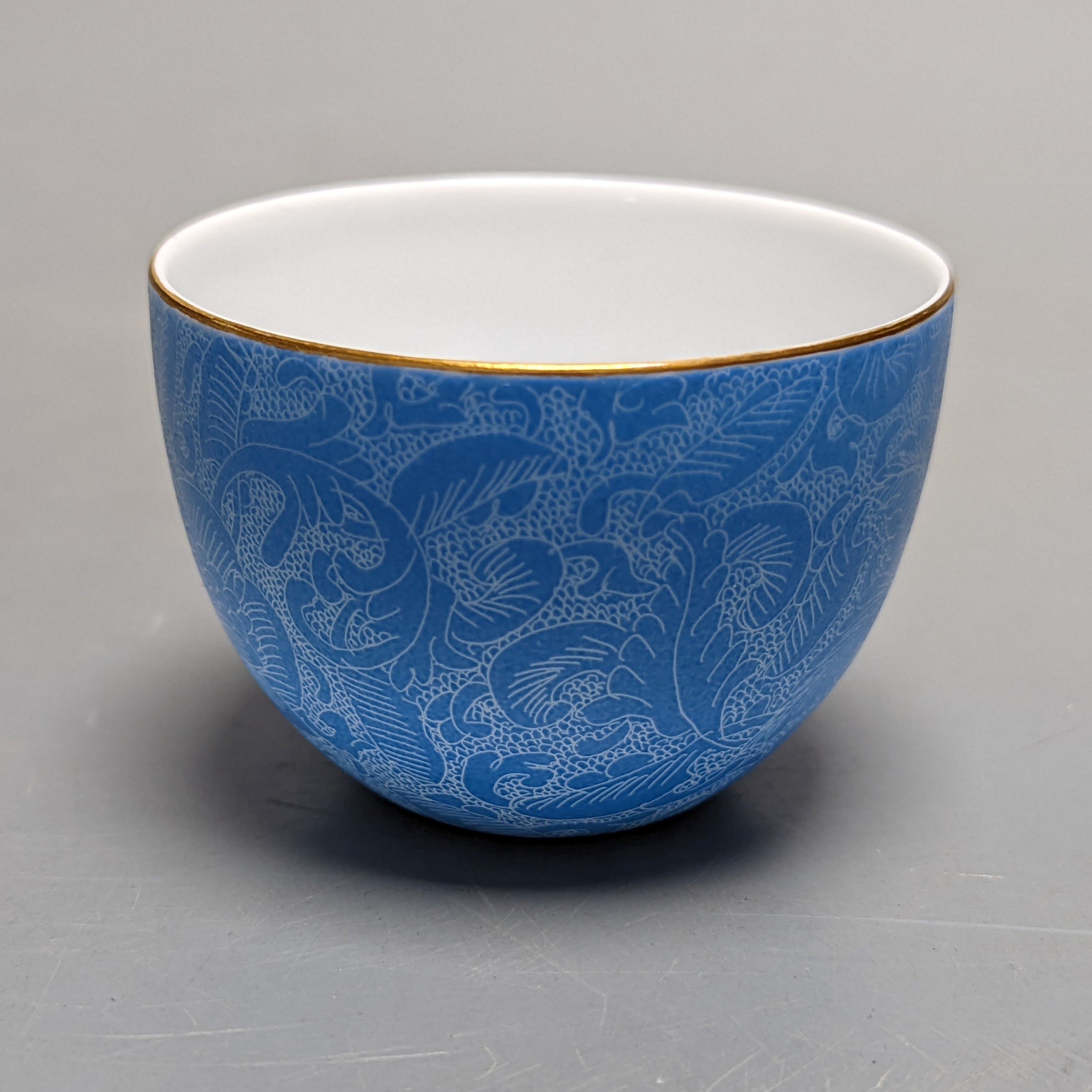 A Japanese or Chinese sgrafitto blue enamelled cup, cased. 6cm diameter