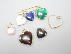 An 18ct safety pin, 47mm, hung with seven assorted heart shaped hardstone pendants or charms, two