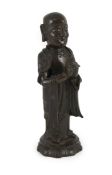 A Chinese Ming bronze figure of a luohan, 17th century,his hands interlocked, standing on a lotus