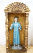 A painted saint with a blue robe and gilt metal halo, standing in an ornate carved niche, 57cm