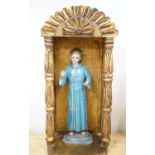 A painted saint with a blue robe and gilt metal halo, standing in an ornate carved niche, 57cm