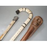 A carved wood figural walking cane, a vertebrae walking stick and a Victorian parasol. Longest