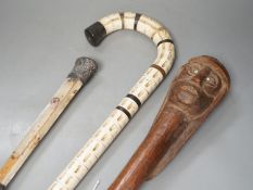 A carved wood figural walking cane, a vertebrae walking stick and a Victorian parasol. Longest