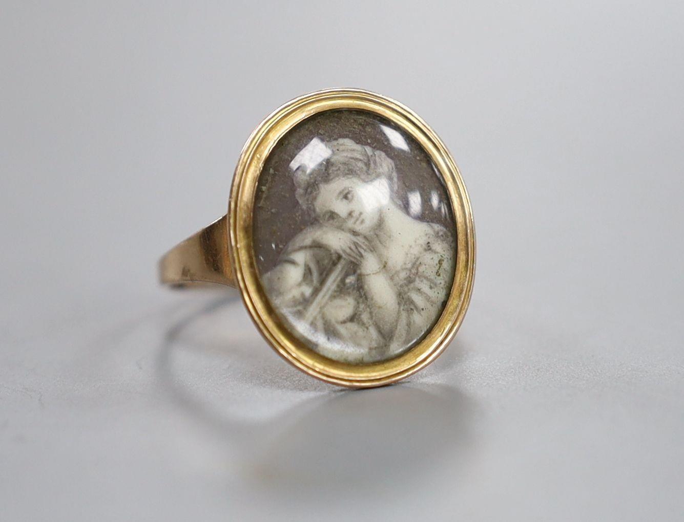 An early 19th century yellow metal ring inset with ivory? panel of a young lady,below a glazed panel