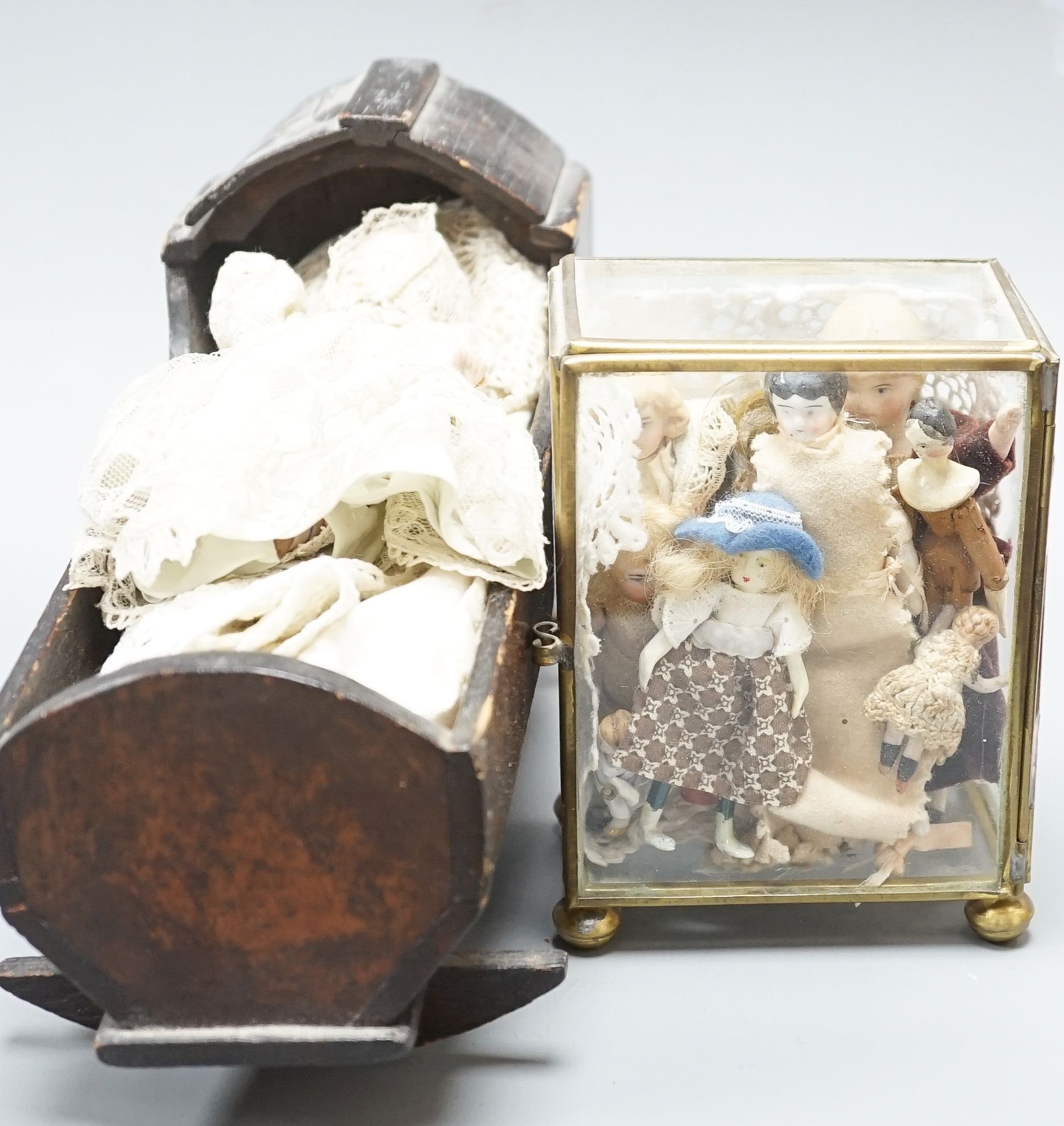 A collection of miniature bisque dolls and another larger doll in a wooden cradle, 11 dolls in