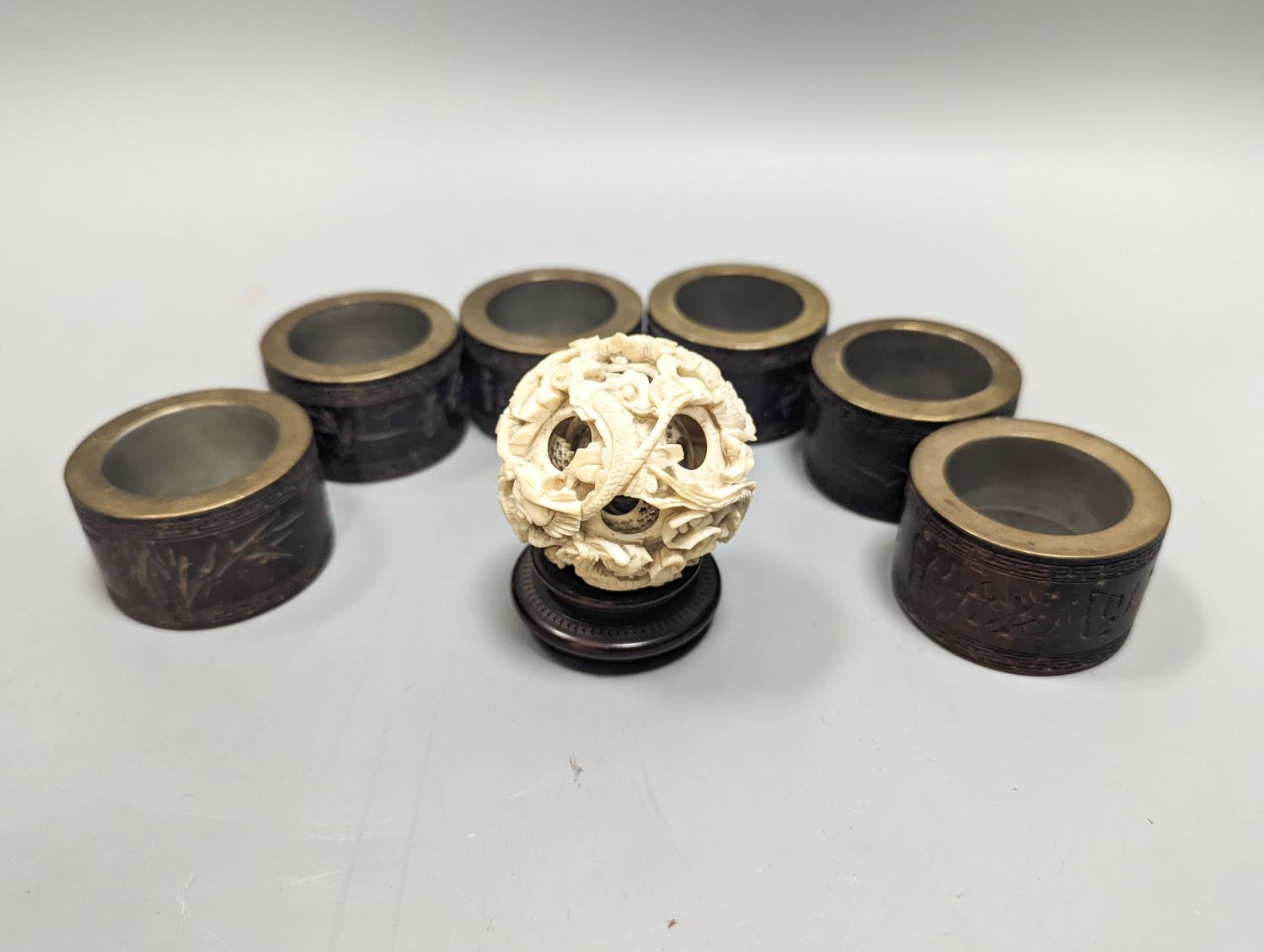 A Chinese ivory concentric puzzle ball, 6 Chinese coconut and brass mounted napkin rings.