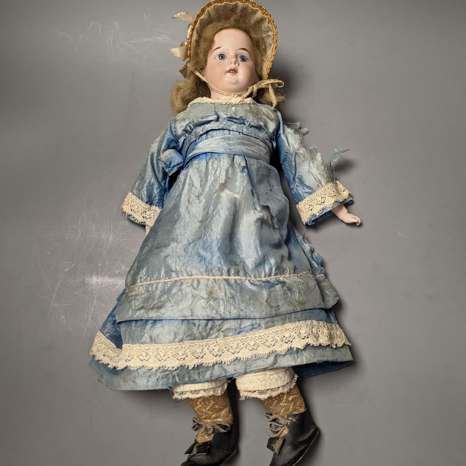 A German bisque headed doll, wearing a blue silk dress and straw bonnet, 42 cms high.