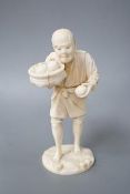 A Japanese carved ivory figure, Meiji period, modelled as a fruit vendor carrying a bowl of fruit in