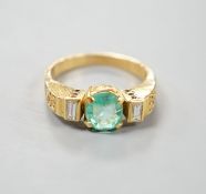 A modern yellow metal, round cut emerald and two stone baguette cut diamond set dress ring, with