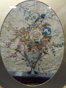 A Georgian oval silk embroidery panel depicting a two handled classical urn containing mixed flowers