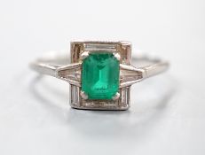 An Art Deco white metal, single stone emerald, baguette and trapeze cut diamond cluster set ring,