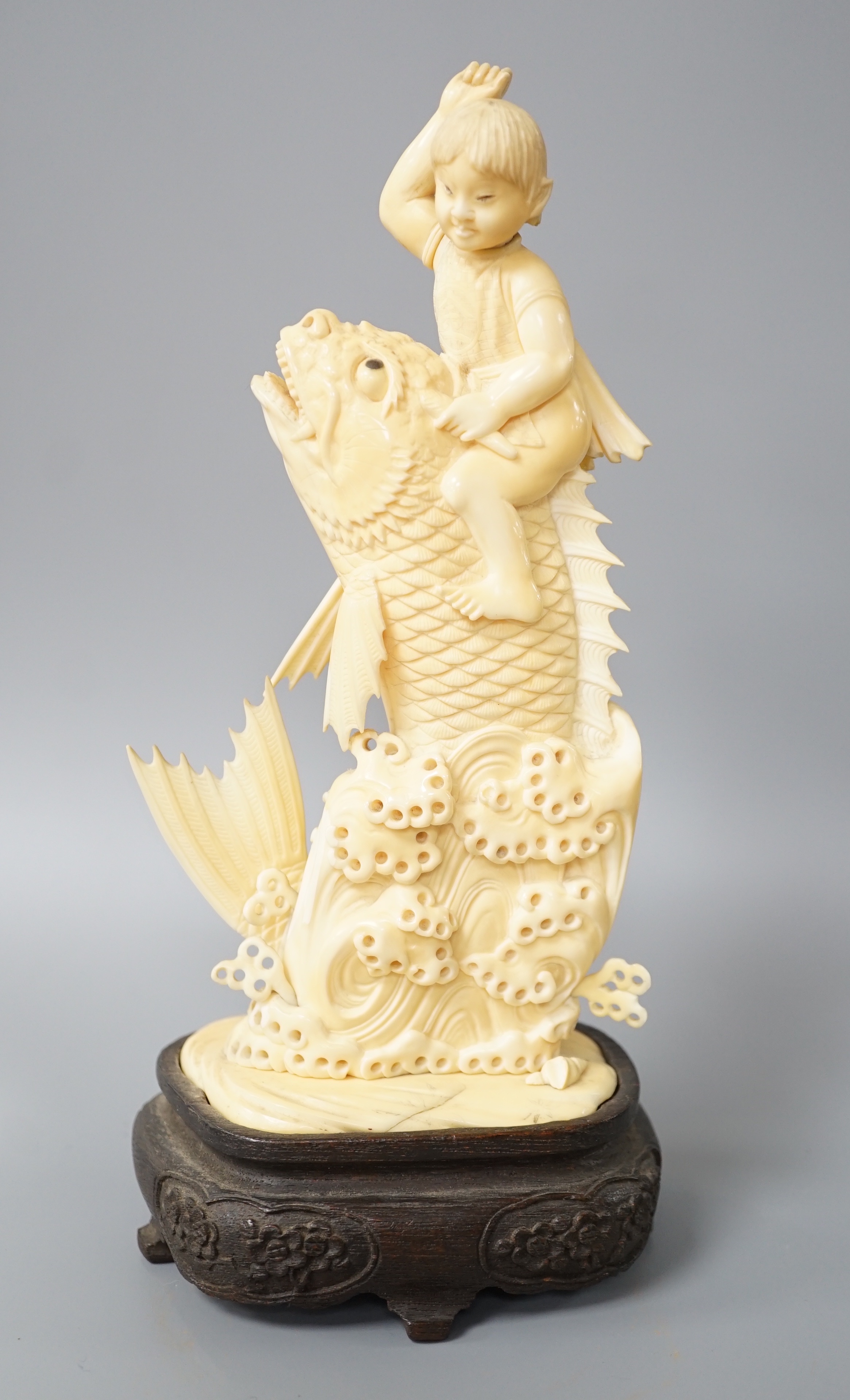 A Japanese sectional ivory okimono of a boy riding a leaping carp, early 20th century, wood stand,
