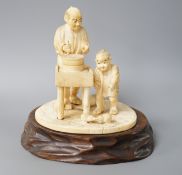 A Japanese ivory okimono of man and boy at a grindstone, Meiji period, signed, wood stand. 15cm