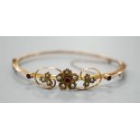 An Edwardian 9ct, red stone and seed pearl set hinged bangle, interior diameter 55mm, gross weight