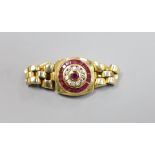 A modern 750, ruby and diamond circular cluster set ring, with articulated shank and clasp, size