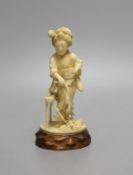 A Japanese Tokyo school carved ivory figure of a woman flailing wheat, Meiji period, wood stand -