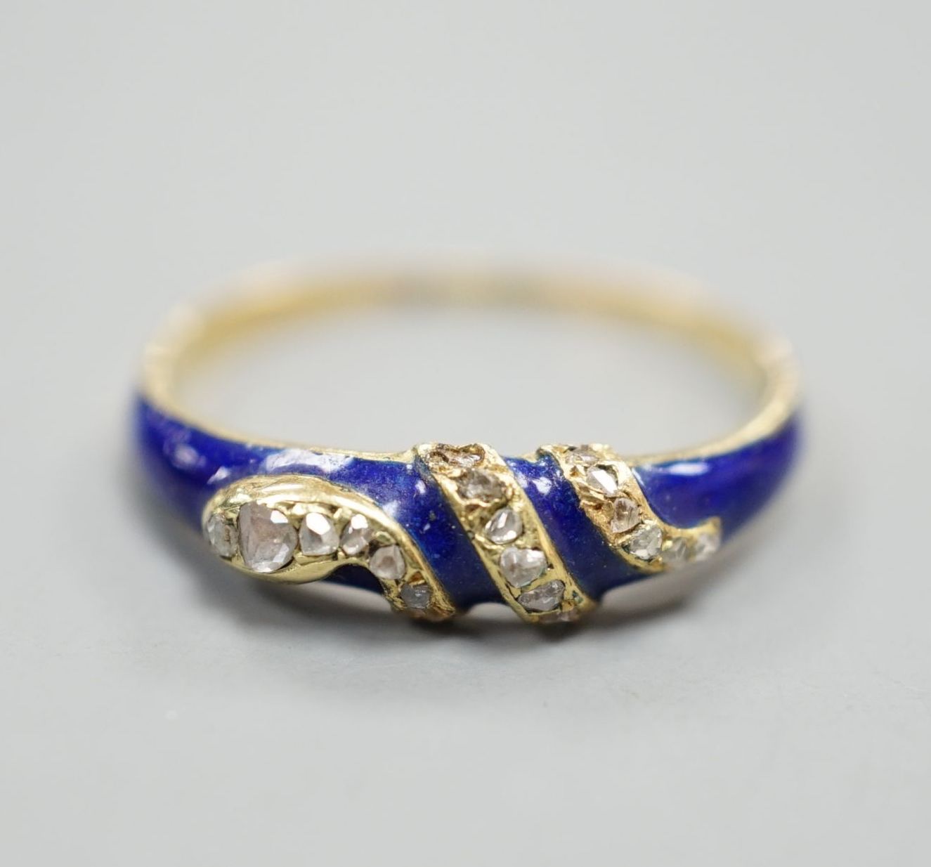 A late Victorian yellow metal, blue enamel and rose cut diamond set serpent ring, size O, gross