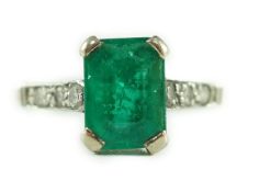 A white gold and single stone emerald ring, with six stone diamond set shoulders, the emerald