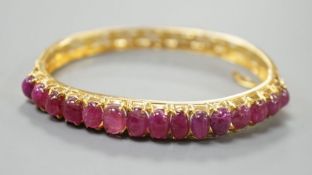 A modern Thai yellow metal and graduated fifteen stone cabochon ruby set hinged bangle, interior