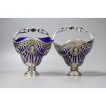 A pair of continental pierced white metal sugar baskets, with shaped blue glass liners, diameter