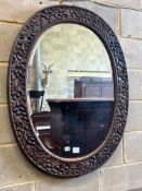 An early 20th century oval oak wall mirror, carved with oak leaves, width 84cm height 106cm