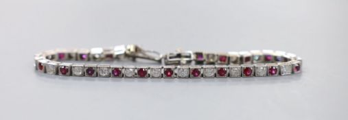 A modern white metal, twenty one stone ruby and twenty three stone diamond set line bracelet, 17.