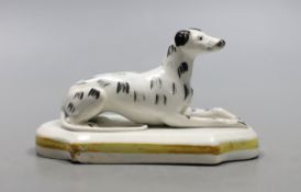 A Staffordshire porcelain model of a recumbent greyhound, c.1830–50, with black markings to its fur,